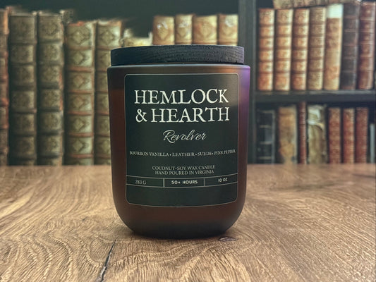 Candle jar labeled 'Hemlock & Hearth' on a wooden surface with bookshelf in the background