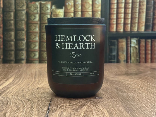 Candle labeled 'Hemlock & Hearth' on a wooden surface with bookshelf in the background