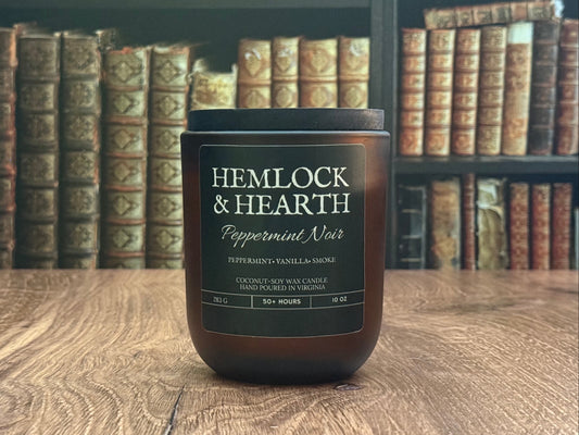 Hemlock & Hearth candle on a wooden surface with bookshelf in the background